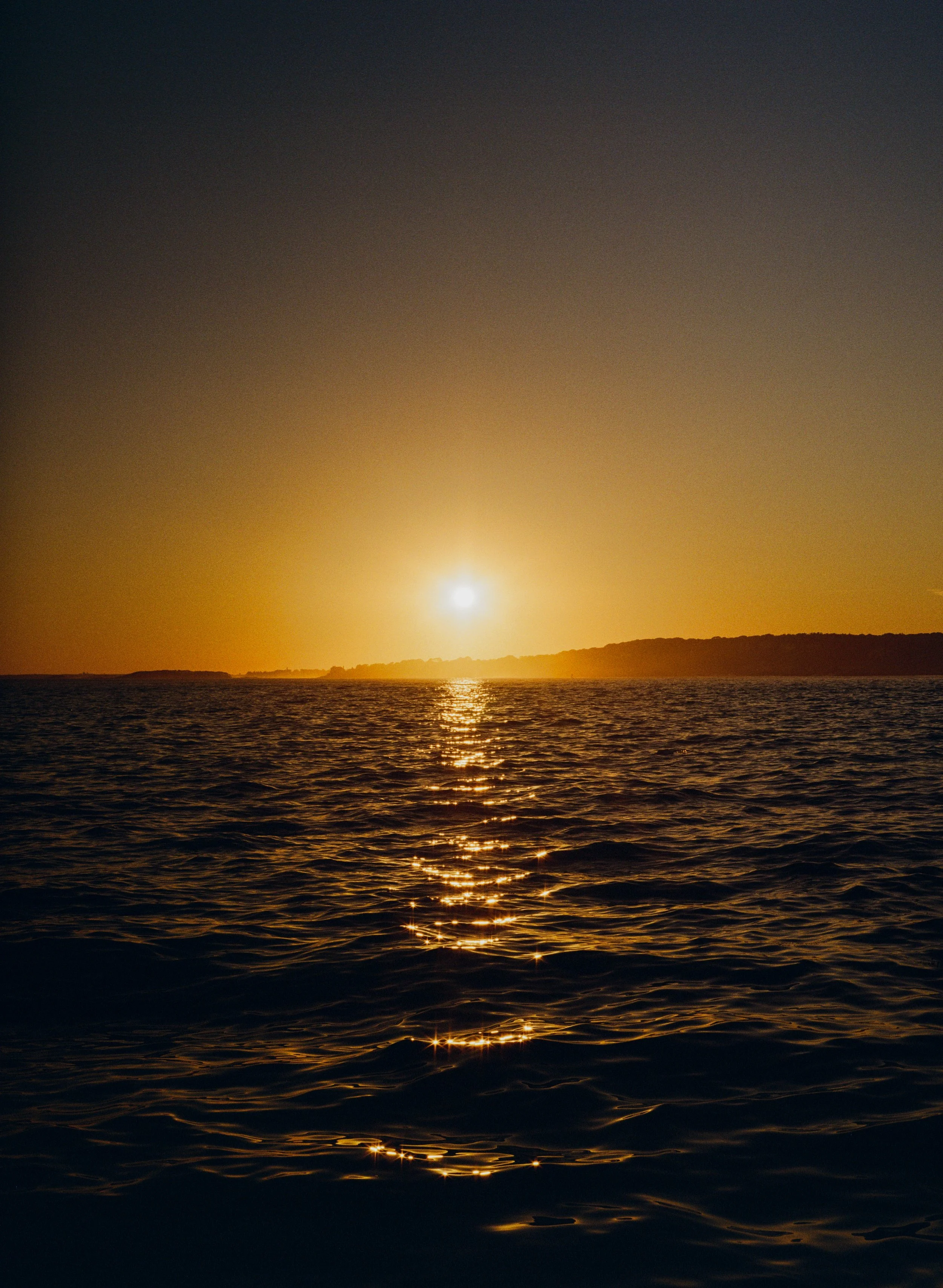 Sunset over a body of water with the sun low in the sky and reflections on the water
