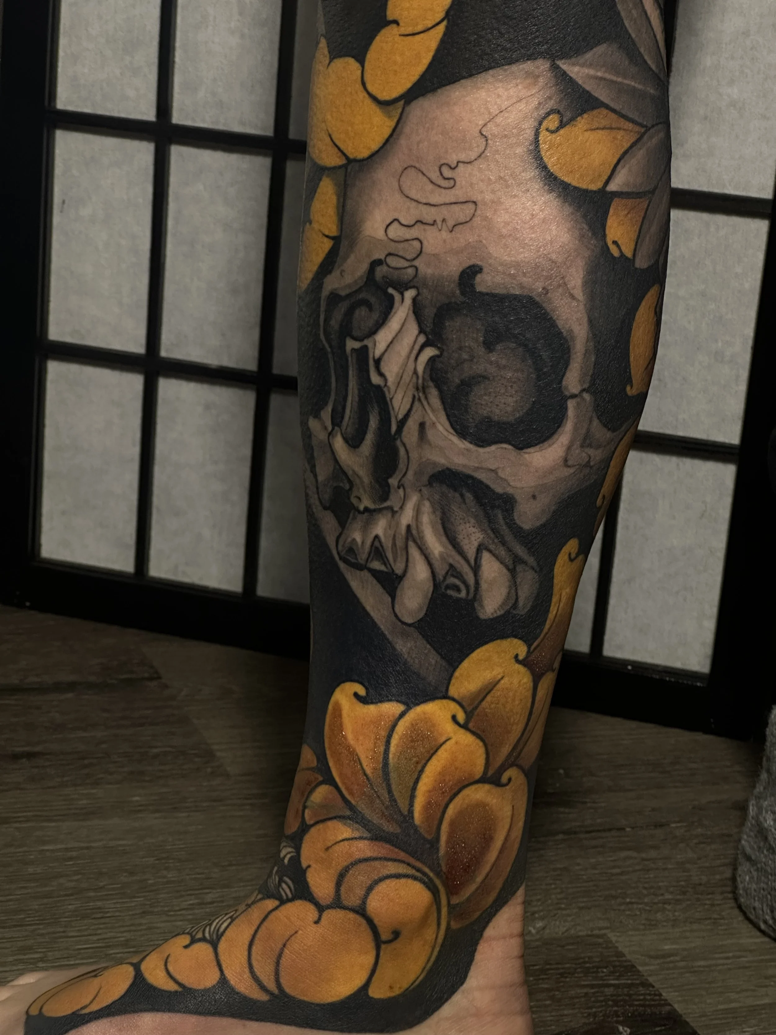 illustrative color and black and gray fusion calf tattoo of a skull surrounded by orange and yellow flowers. tattoo by edgar.tattoos in colorado