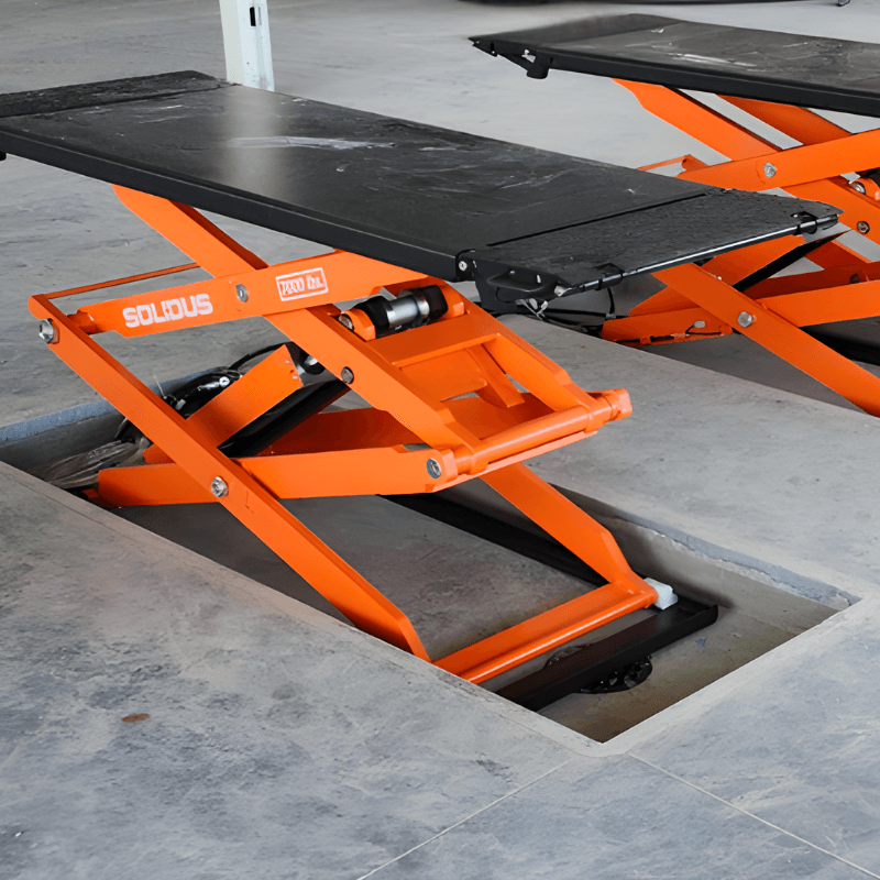 An orange hydraulic scissor lift table used in auto body collision shops