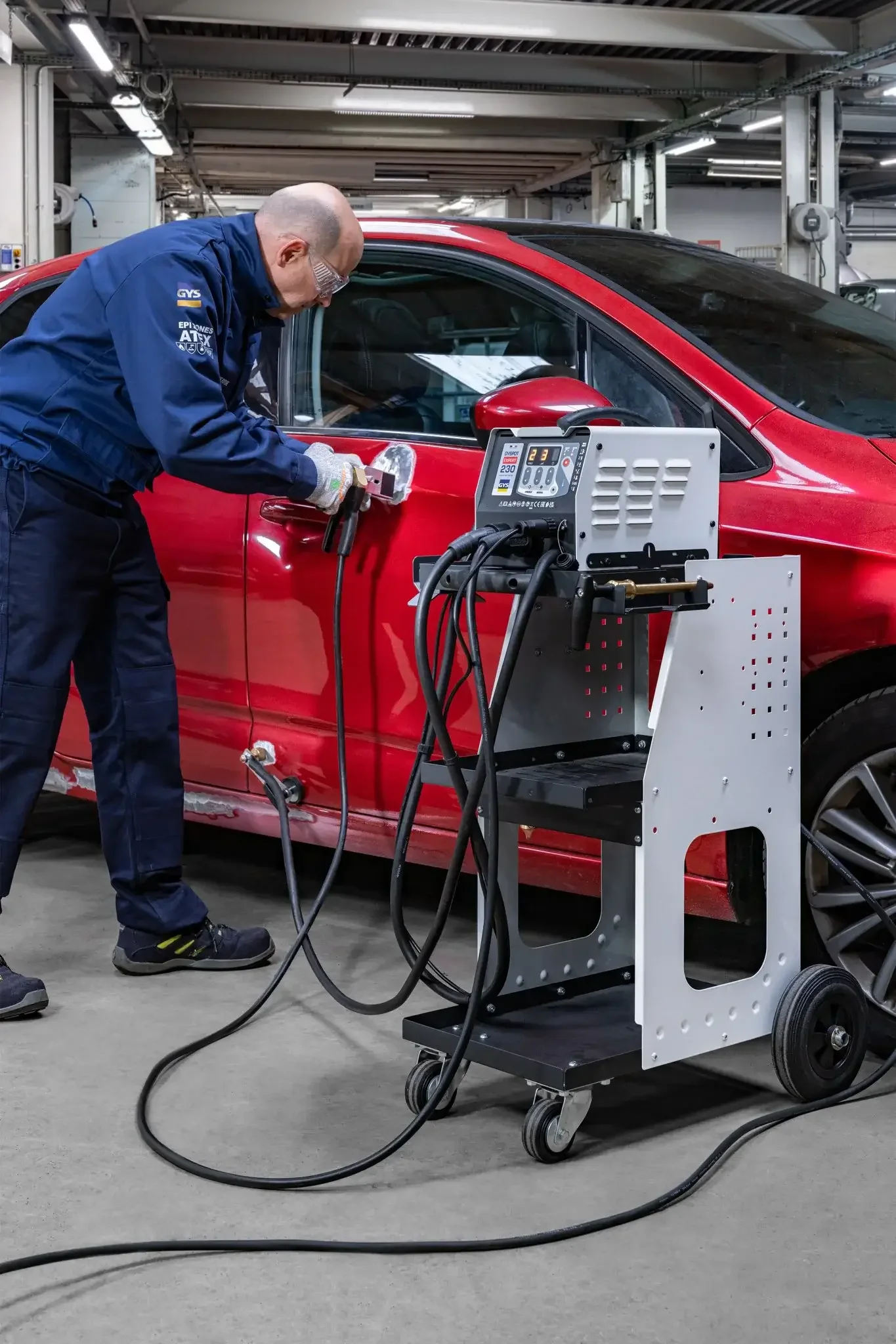Tech using a gys dent puller to remove dents in a red car