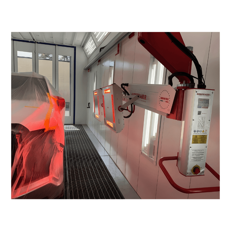 Automobile undergoing a paint curing process in a specialized paint booth with infrared heating lamps.