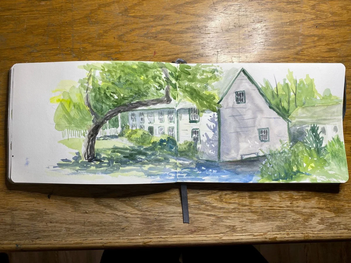 Watercolor painting of a house with a tree and greenery in a garden, on a wooden surface