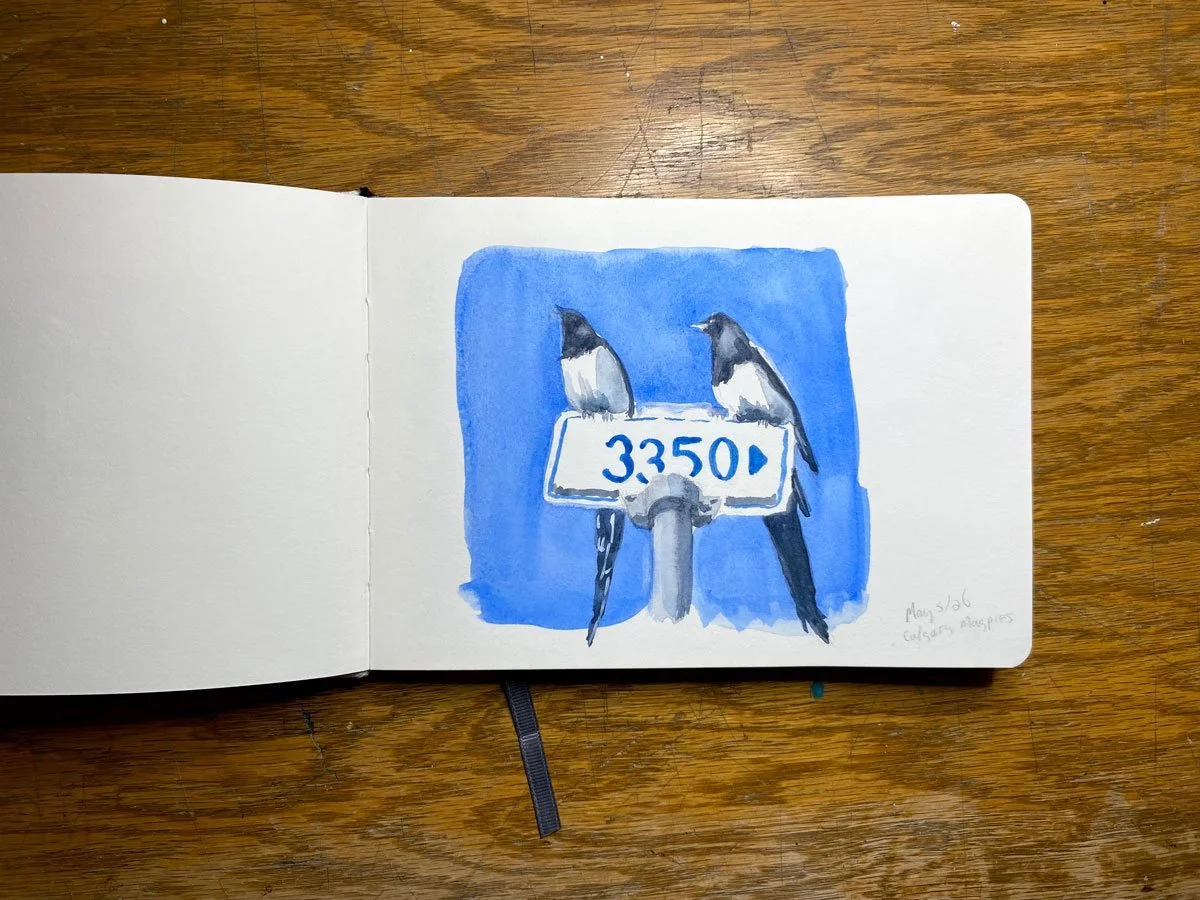 Watercolor illustration of two birds perched on a street sign that reads '3.350'. The background is blue, and the scene is drawn in a sketchbook on a wooden surface.