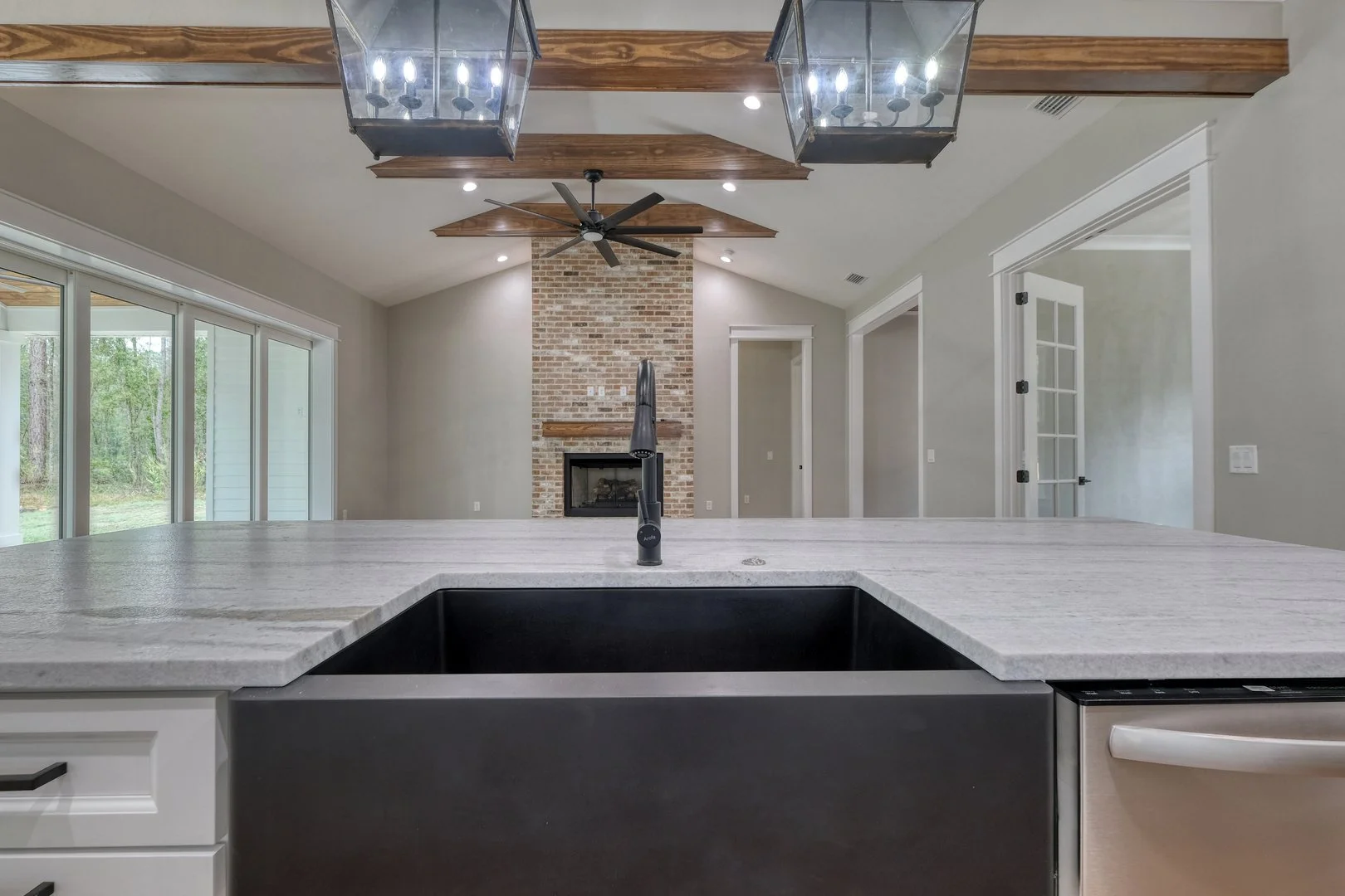 Modern kitchen with large island, black sink, granite countertops, and open living area with brick fireplace and ceiling fan.