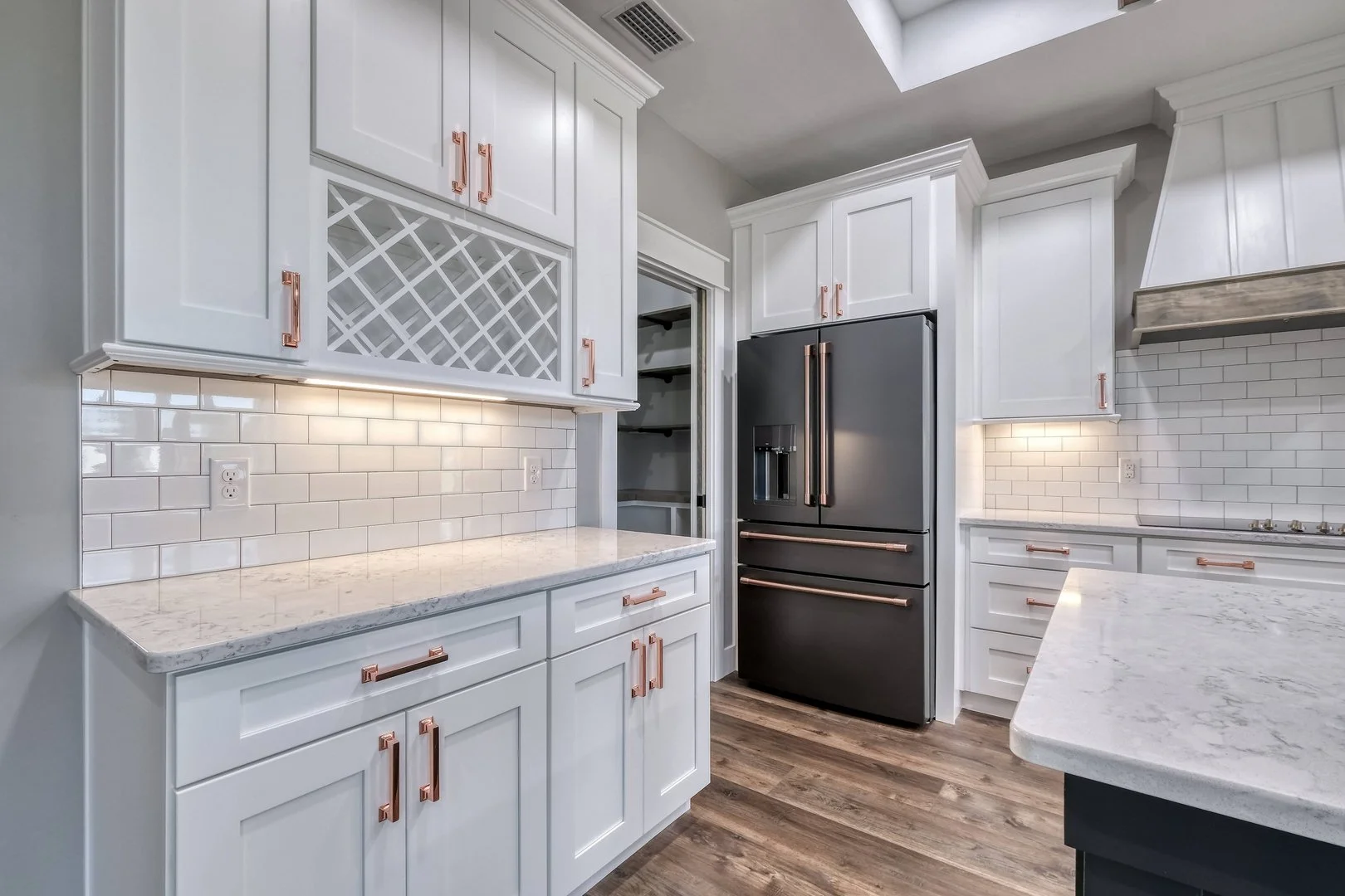 Modern kitchen with white cabinets, marble countertops, black refrigerator, and white subway tile backsplash, hardwood flooring, and under-cabinet lighting.