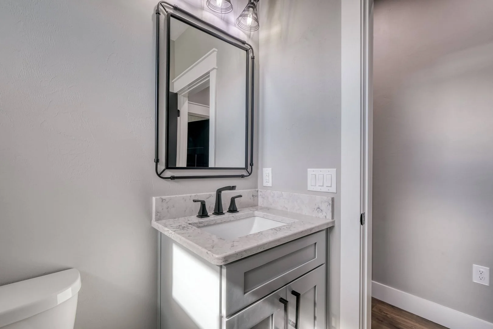 Modern bathroom vanity with marble countertop, black fixtures, white cabinet, mirror with black frame, and wall-mounted light fixtures.