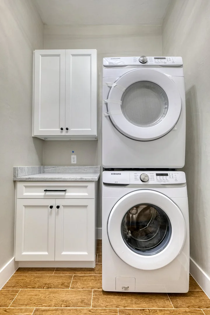 Laundry room with a stackedSamsung washer and dryer, white cabinet, and a granite countertop on wooden flooring.