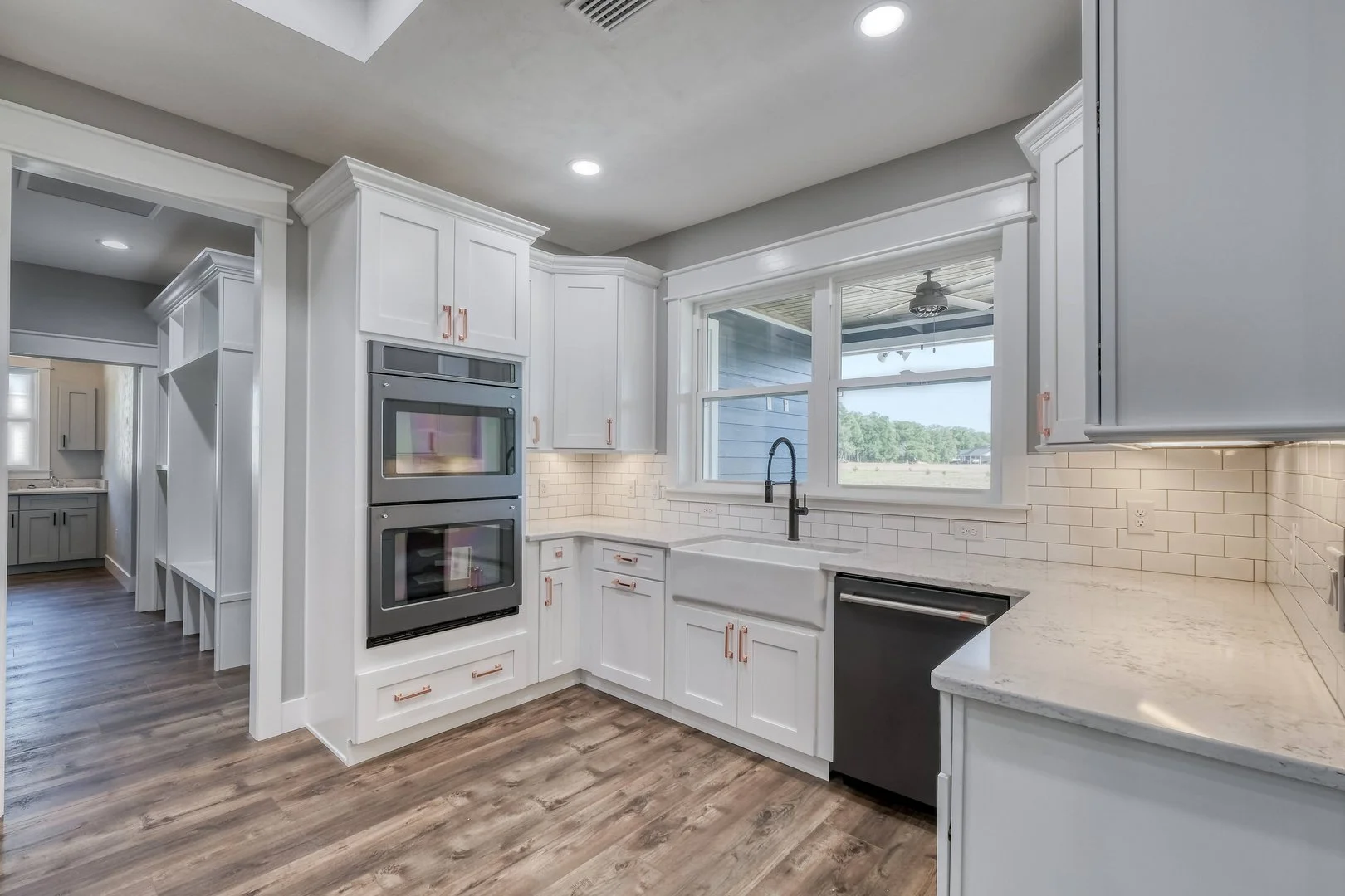 Modern kitchen with white cabinets, a large window above the sink, and dark wood flooring.
