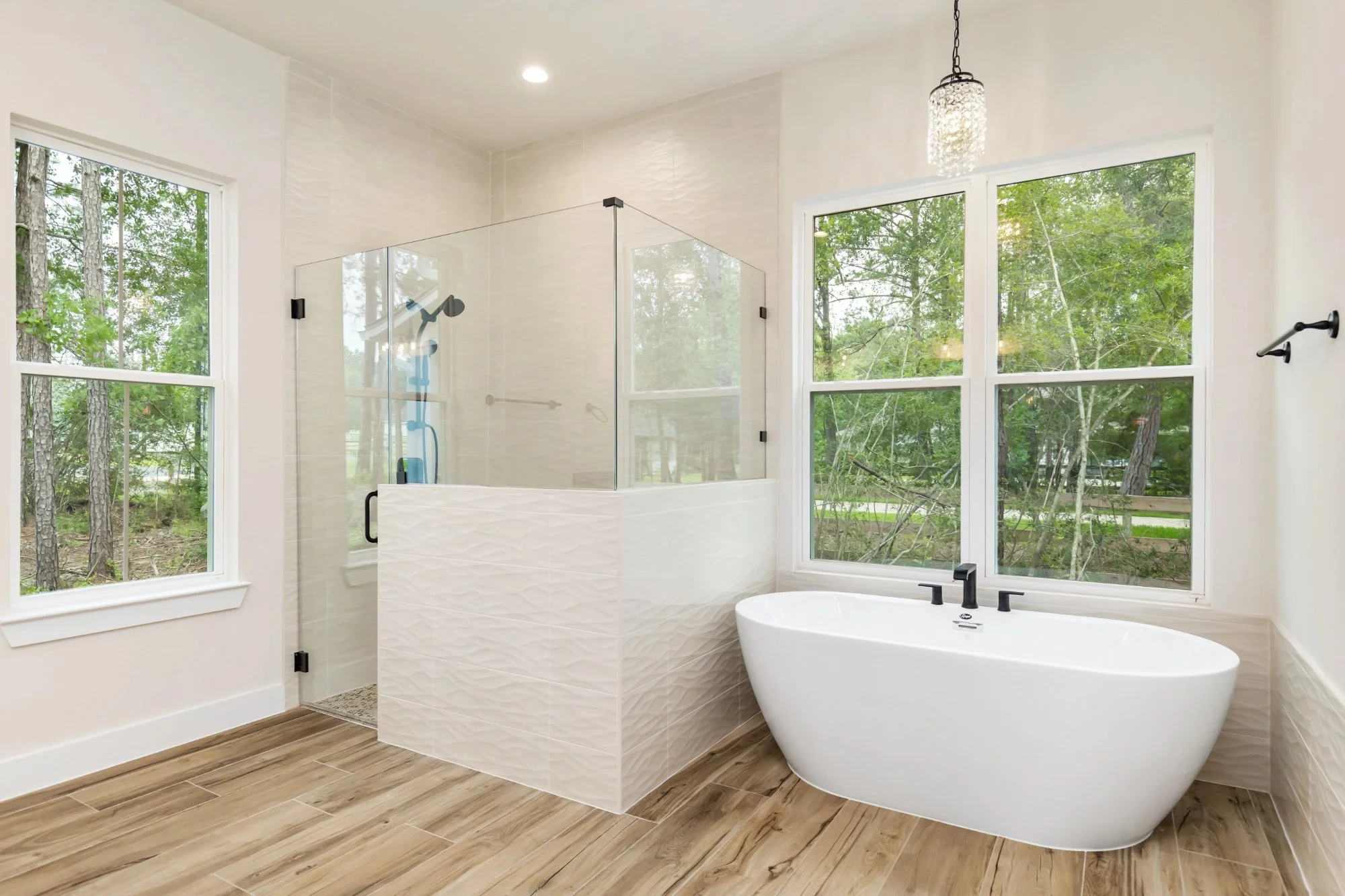 Modern bathroom with a walk-in shower with glass enclosure and a freestanding bathtub next to large windows showing trees outside.