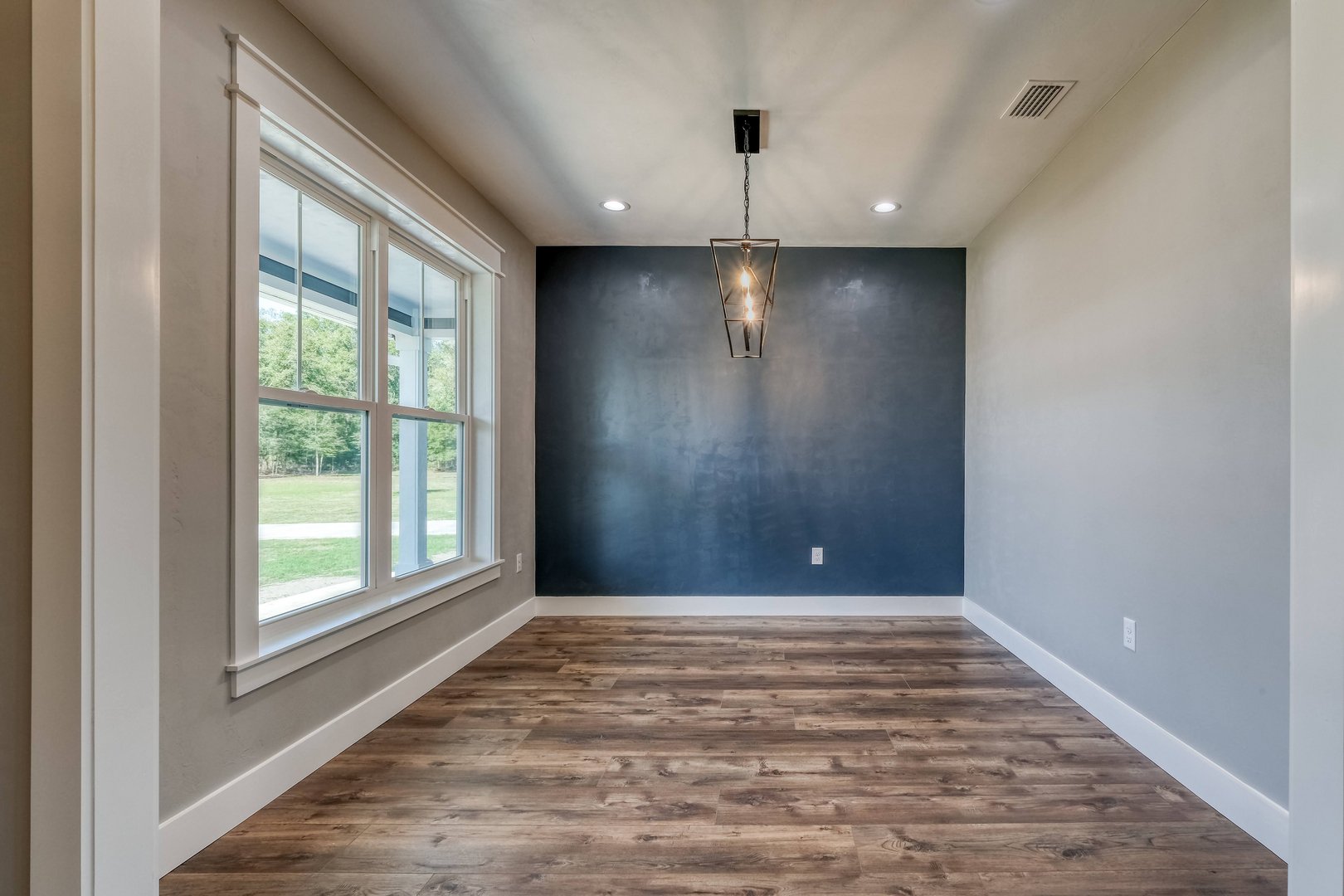 Empty room with large window, blue accent wall, and wood flooring.