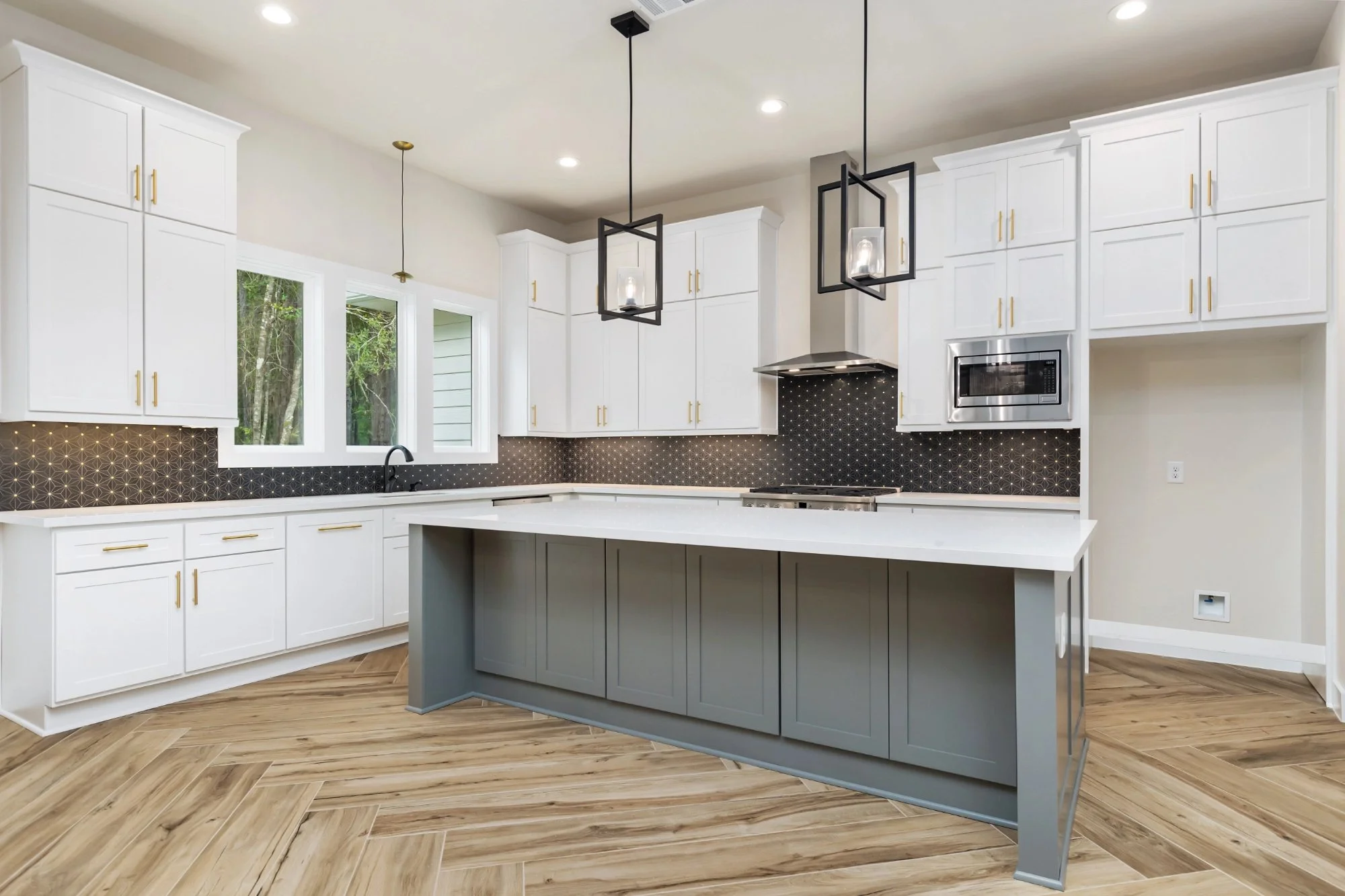Modern kitchen with white cabinets, black backsplash, and gray island, pendant lights, and wood-look tile flooring.