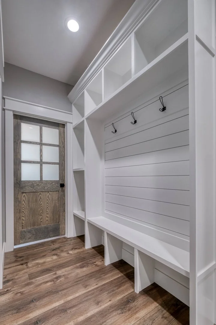 A small mudroom or entryway with a wooden door, white built-in storage with hooks, and shelving.