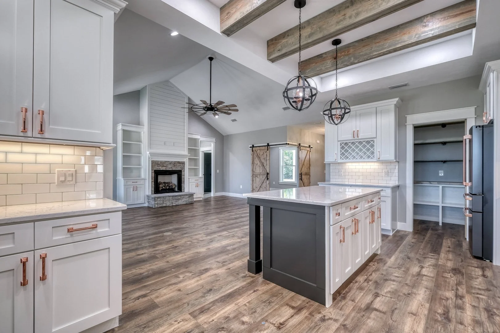 Open-concept kitchen and living area with white cabinets, wooden accents, and a stone fireplace