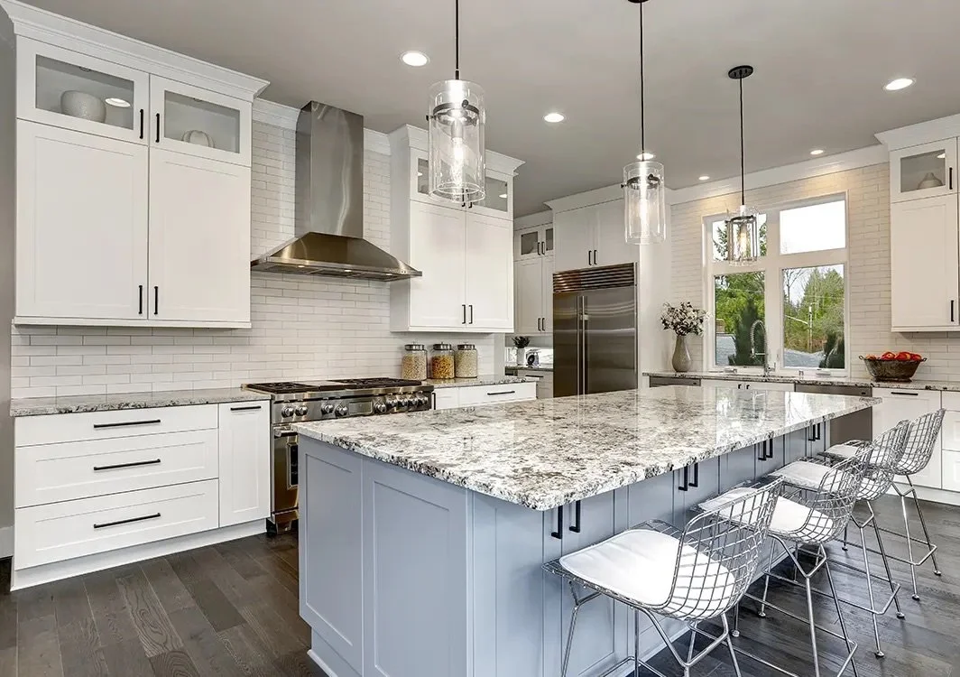 Modern kitchen with white cabinets, granite island, stainless steel appliances, pendant lighting, and large window overlooking greenery.