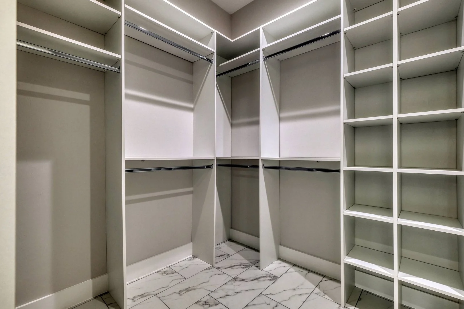 Empty walk-in closet with white built-in shelves and marble tile floor.