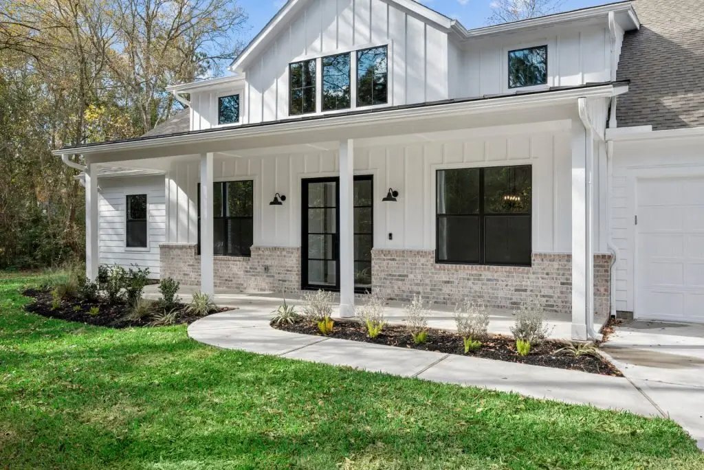 Front view of a modern two-story house with white siding, black window frames, and brick accents, surrounded by a well-maintained lawn and landscaping.