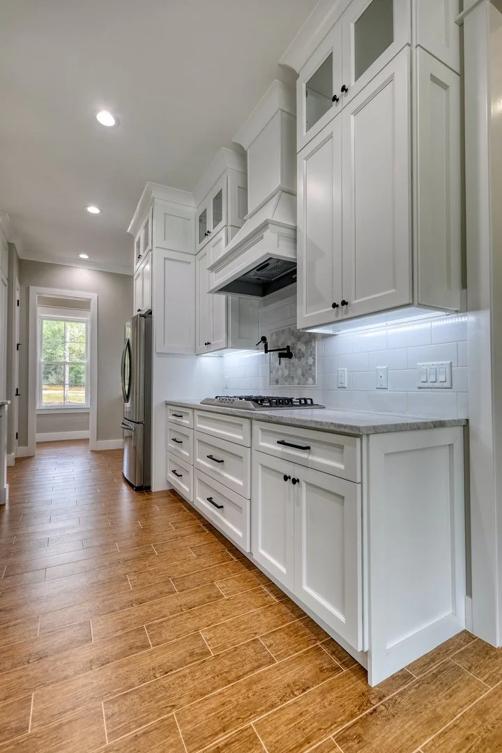 White kitchen with upper and lower cabinets, a gas stove, and a stainless steel refrigerator. Wood flooring and recessed lighting.