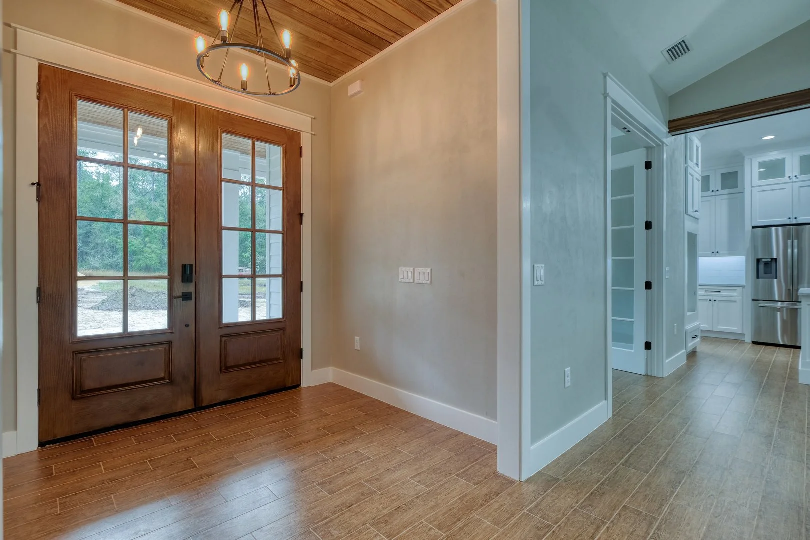 Entryway with wooden double doors leading outside and a view of the yard, hardwood floors, and a modern chandelier hanging from a wooden ceiling.