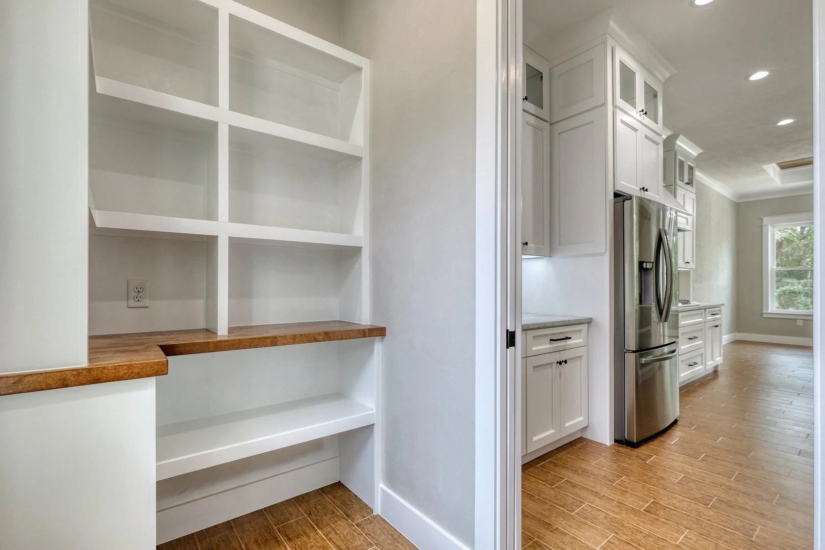 Kitchen with white cabinetry and stainless steel refrigerator, wooden flooring, and empty built-in shelves with a wood countertop.