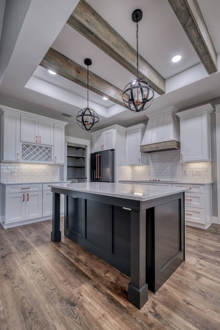 Modern kitchen with white cabinets, a black island, wood flooring, and two spherical pendant lights hanging from a ceiling with exposed wooden beams.