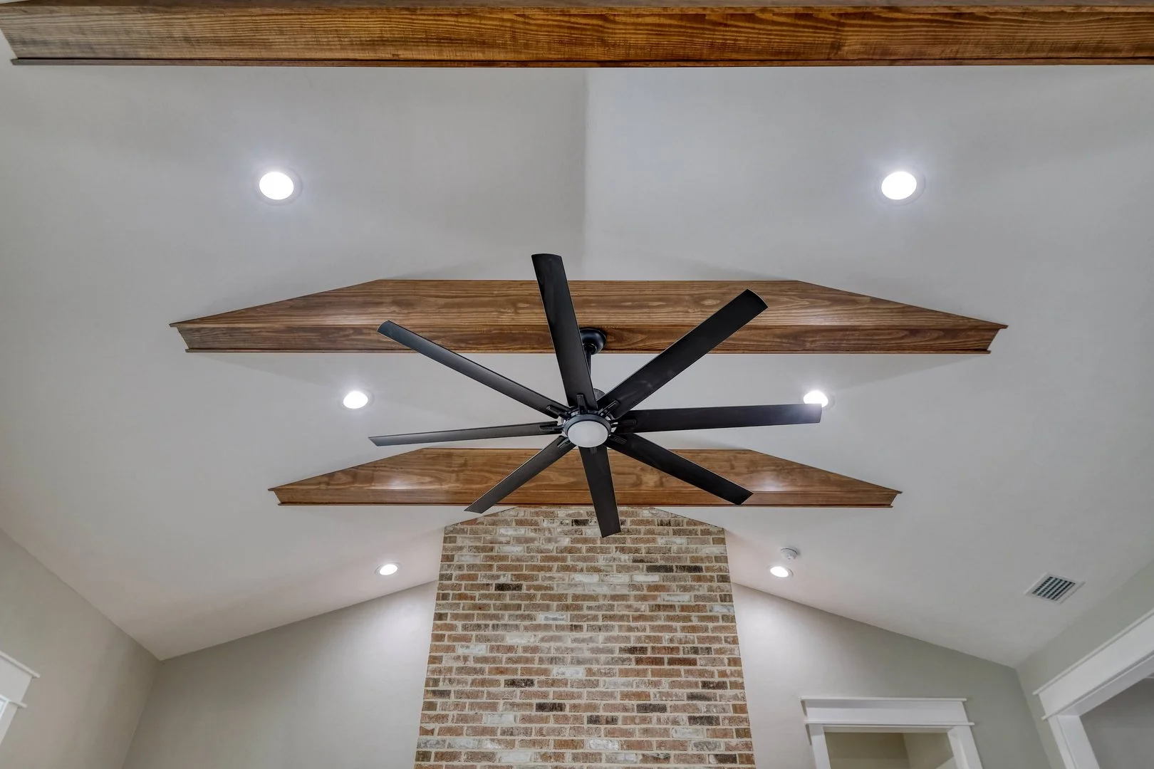 Ceiling with four recessed lights, a black ceiling fan with multiple blades, and two wooden beams.
