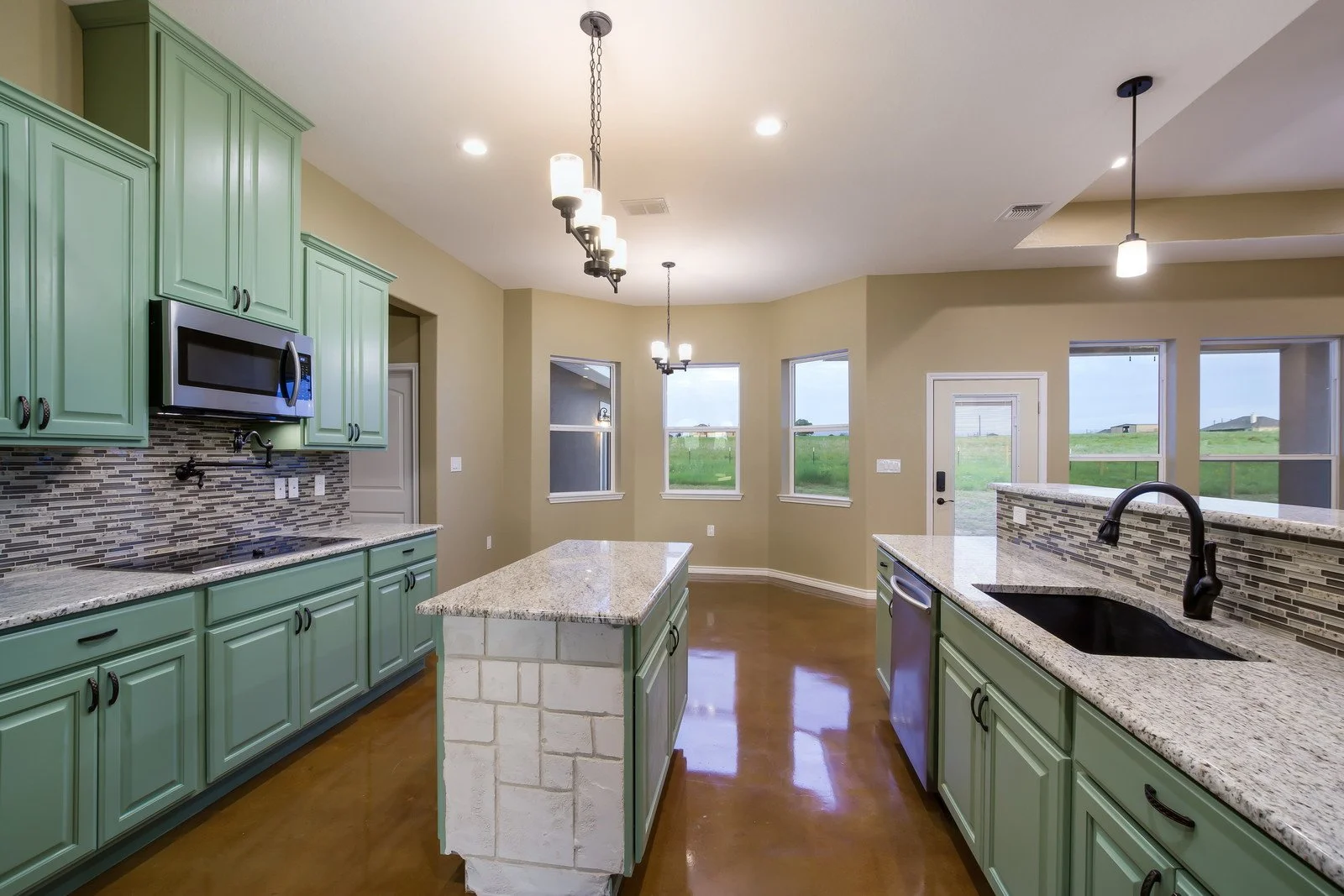 Modern kitchen with mint green cabinets, granite countertops, a small island with a white brick base, a black sink, and city views through multiple windows.