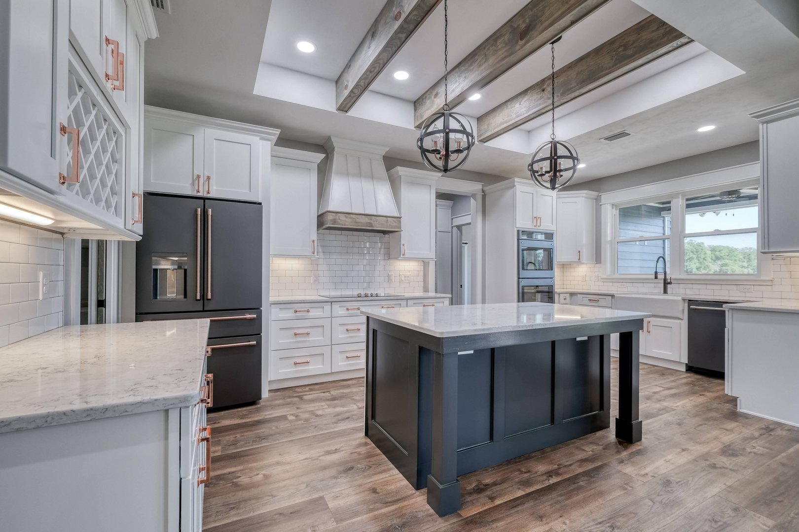 Modern kitchen with white cabinets, a black kitchen island, stainless steel appliances, wood flooring, and a skylight with decorative chandeliers.