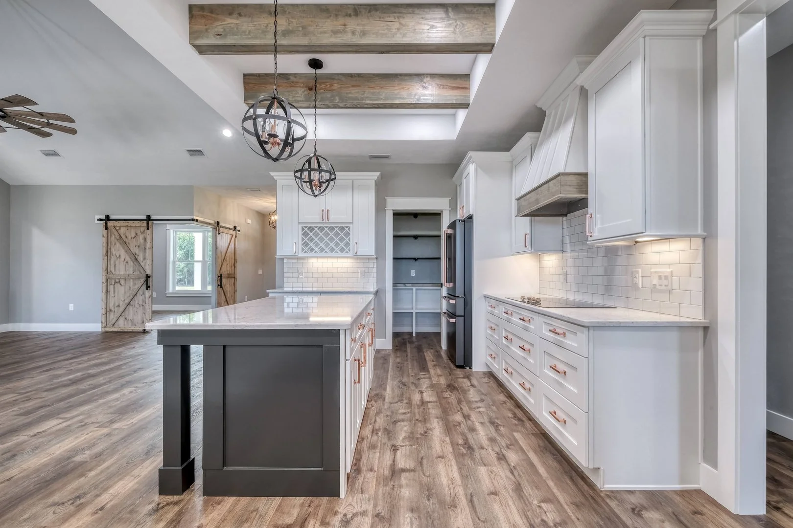 Modern kitchen with white cabinets, wooden accents, and pendant lights over island, with open floor plan leading to a barn door and living area.