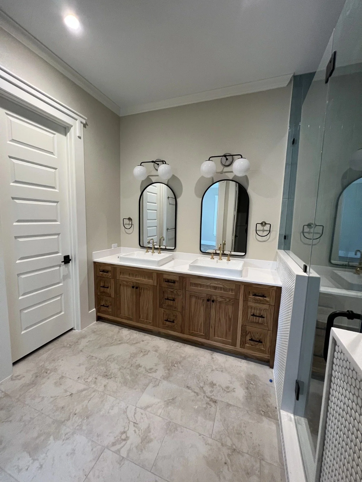 Bathroom with double vanity, two mirrors, two light fixtures, and a shower with a glass door.