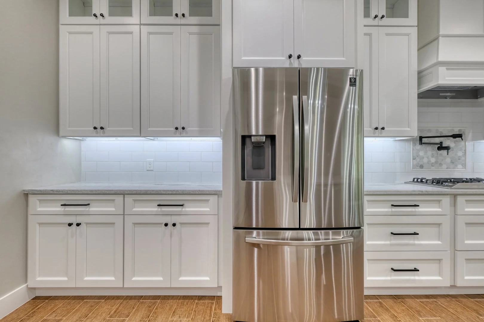 Modern kitchen with white cabinets and a stainless steel refrigerator with water and ice dispenser, wood flooring, and tiled backsplash.