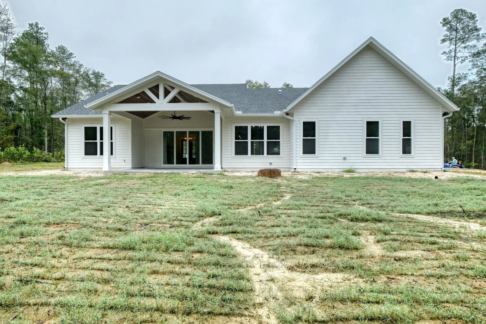 Newly constructed white house with a covered patio, sliding glass doors, and multiple windows, surrounded by a grassy yard and trees.