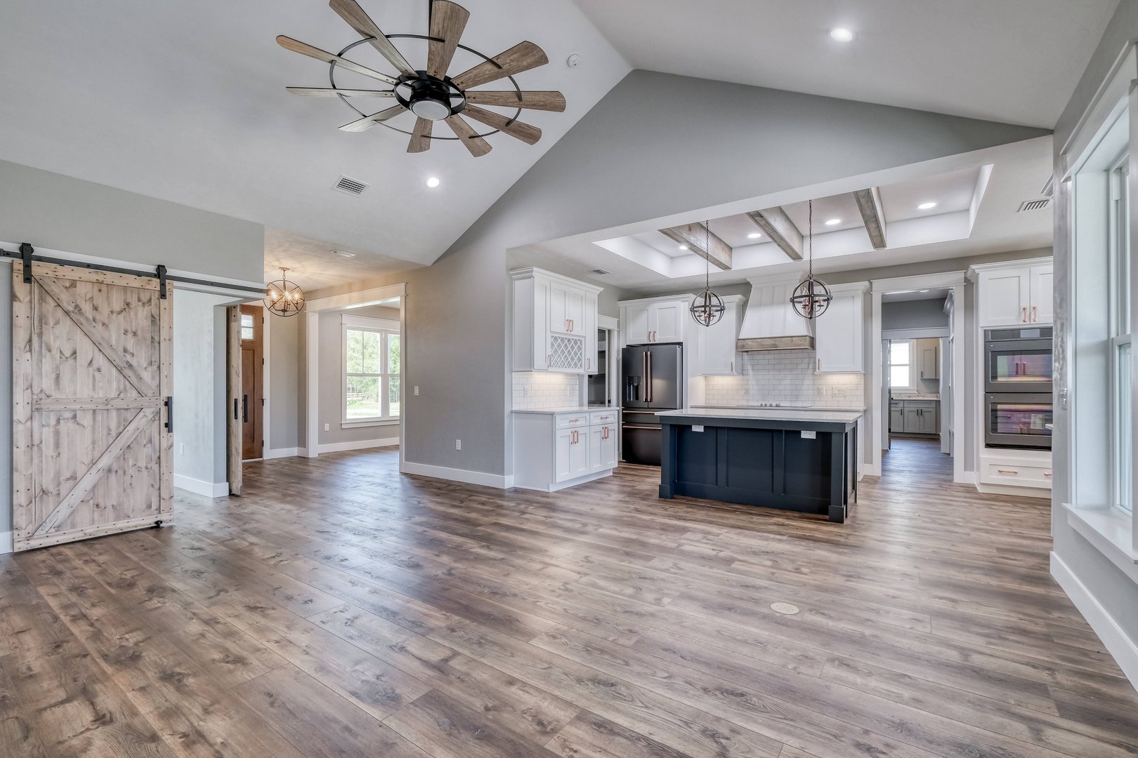 Open-concept kitchen and living space with wood floors, white cabinets, black appliances, and modern lighting fixtures in a new home.