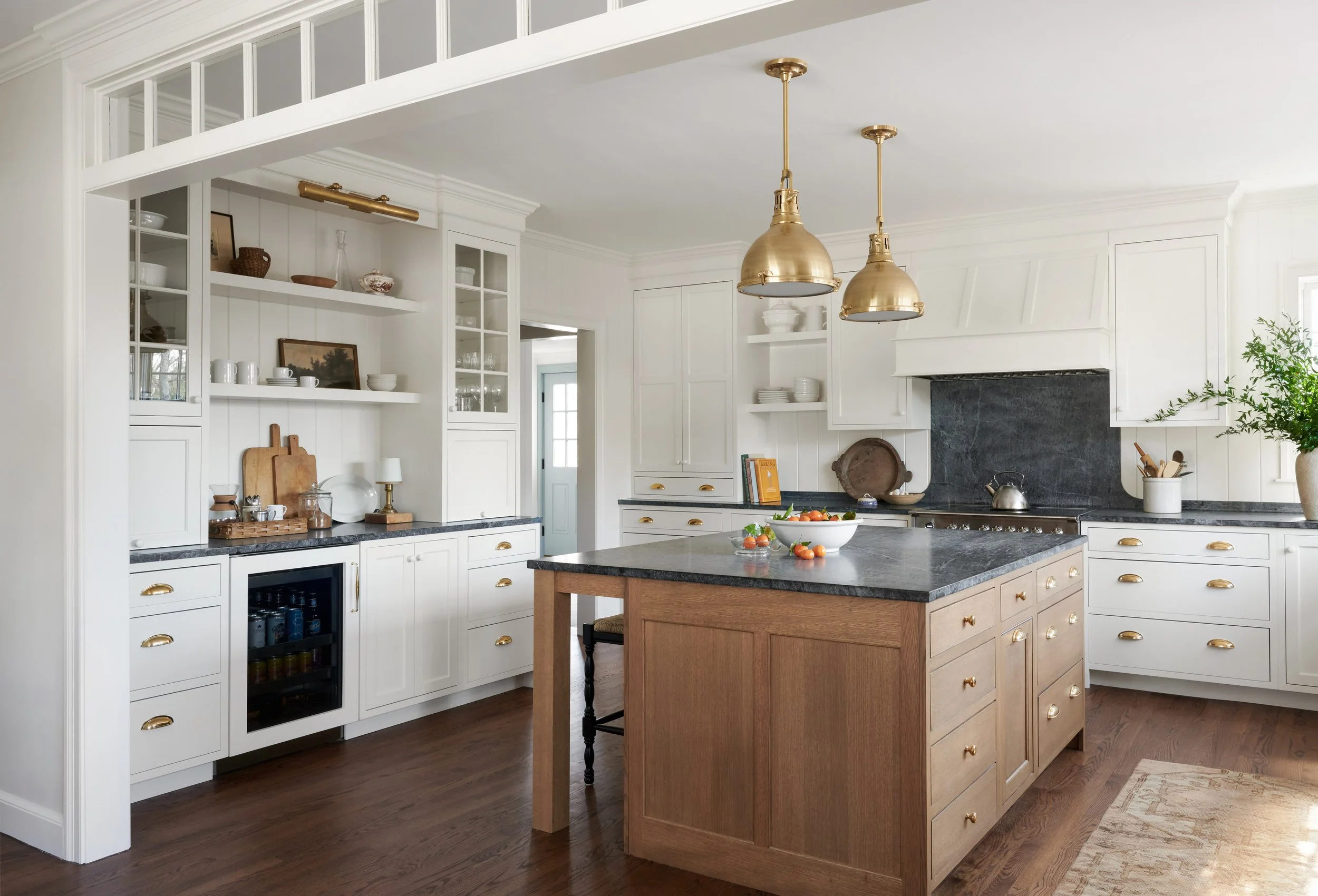 Kitchen with white cabinets, black countertops, a central wooden island, and two gold pendant lights hanging over the island. Open shelves display dishes and decorative items, and a bowl of strawberries and tomatoes is on the island.