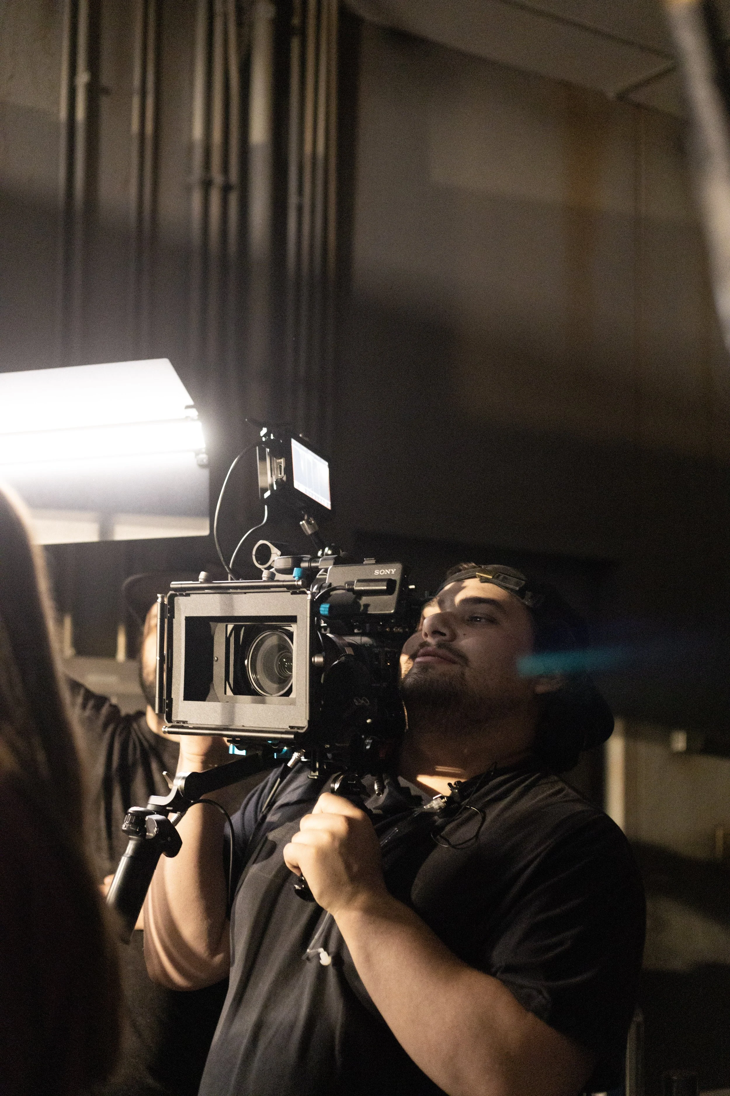 A man operating a professional film camera on a set, with studio lighting and dark background.
