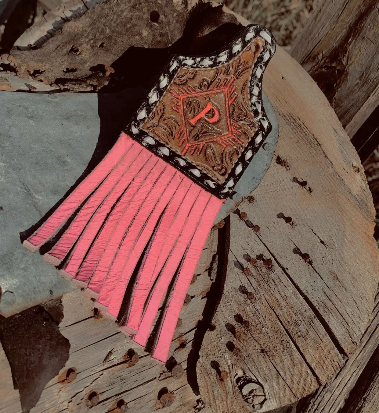 A decorative sheriff's badge with a fringed pink leather strap on a rustic wooden surface.