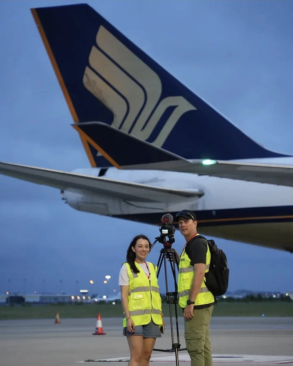Julia and Gavin in hi-vis streaming beside a Singapore Airlines Boeing 747 tail
