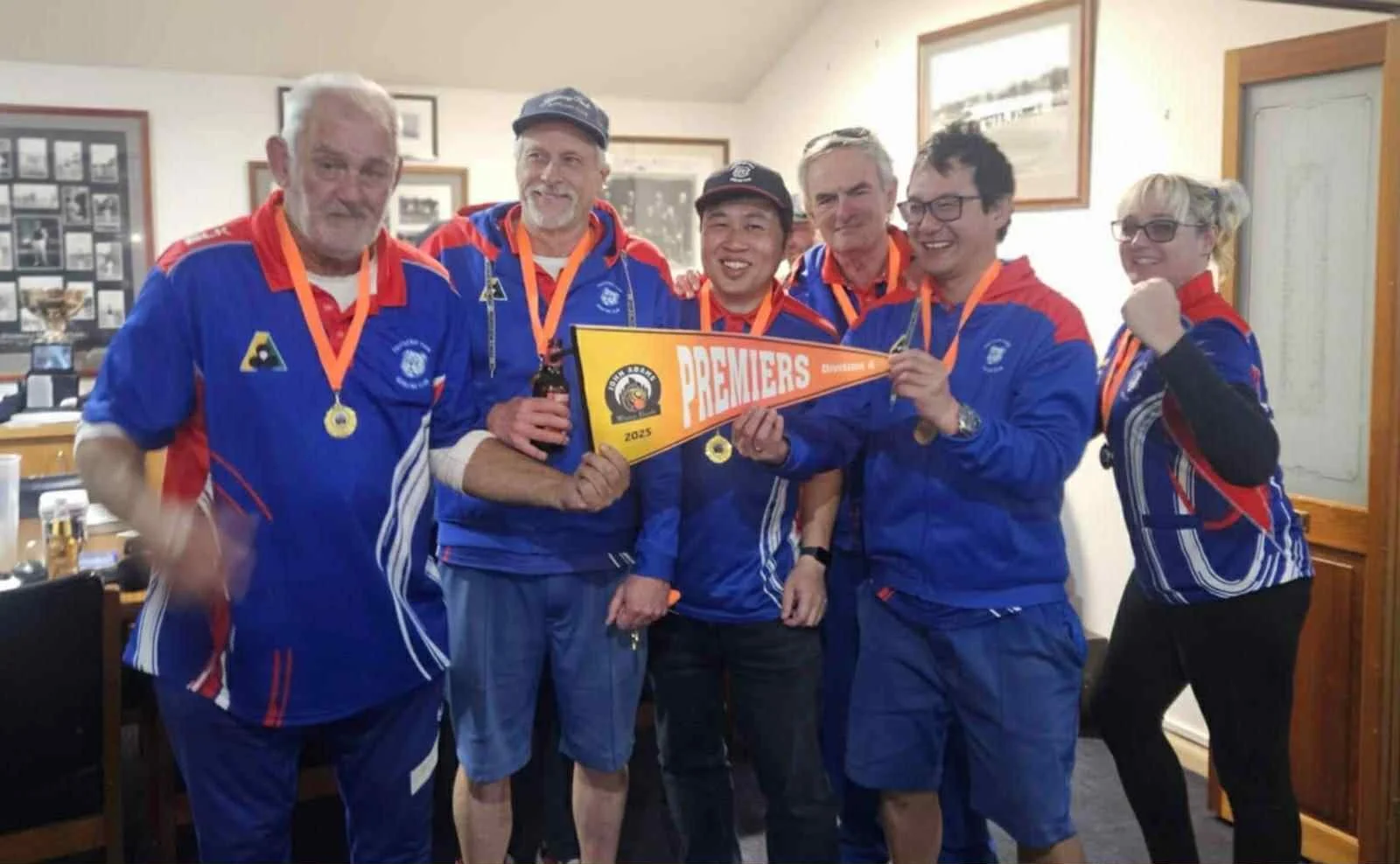 Footscray Park Bowling Club team celebrating indoors, wearing club uniforms with medals and holding a winners pennant
