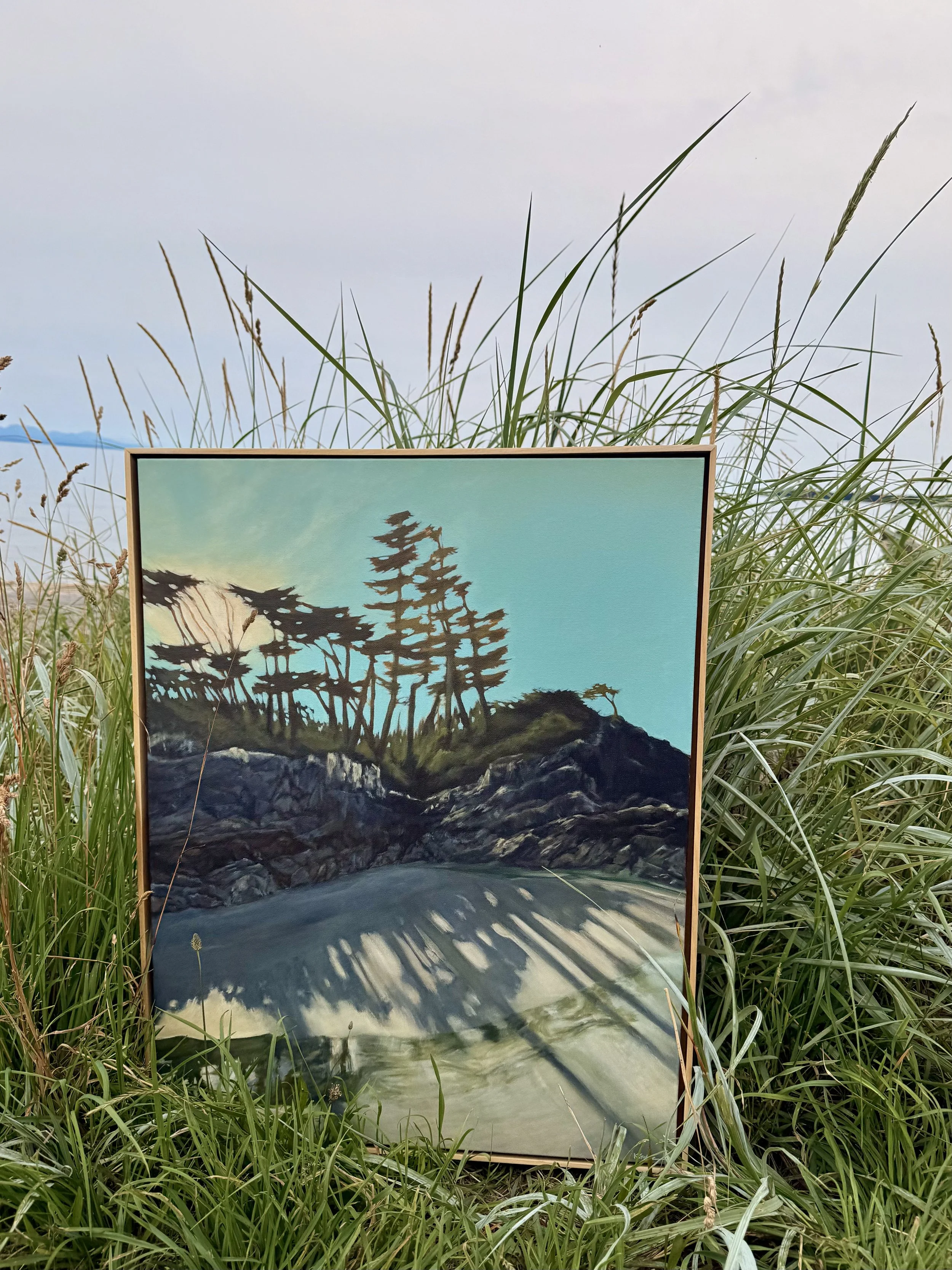 Painting of trees on a rocky coastline, with a body of water in the foreground, set outdoors among tall grass.
