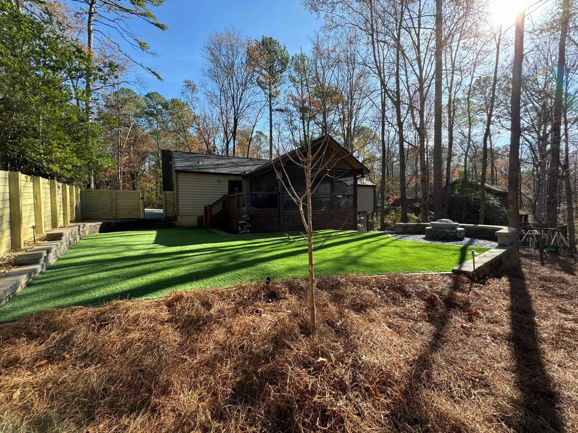 artificial green turf in a home's backyard with a fence and stone retaining wall surrounding the turf featuring outdoor firepit