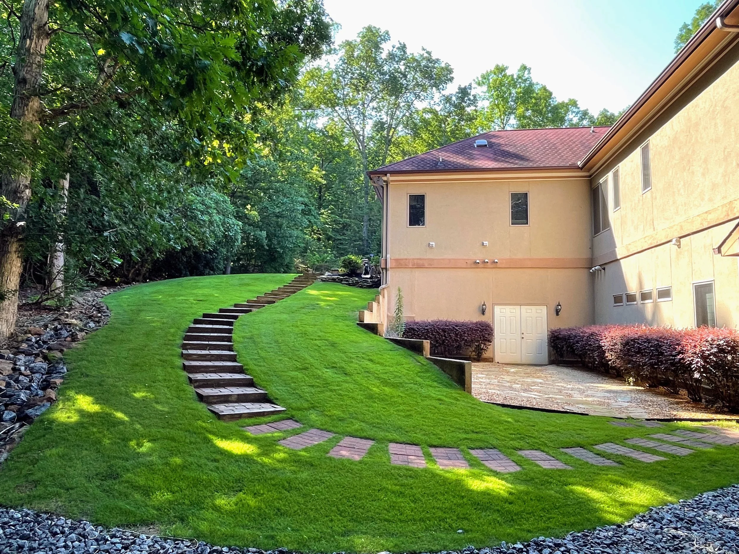 Sloping hill on side of a residential home featuring freshly insalled zeon sod that is bright green and lush. Paver steps were installed leading from the driveway down to the side of the house with a featured gravel sitting patio.