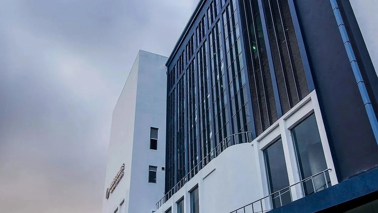 View of modern multi-story office building with dark blue and white exterior, glass windows, and cloudy sky in the background.