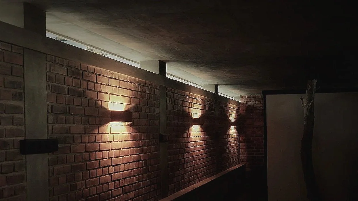 Pattern of wall-mounted lights casting X-shaped shadows on a brick wall in a dimly lit space.