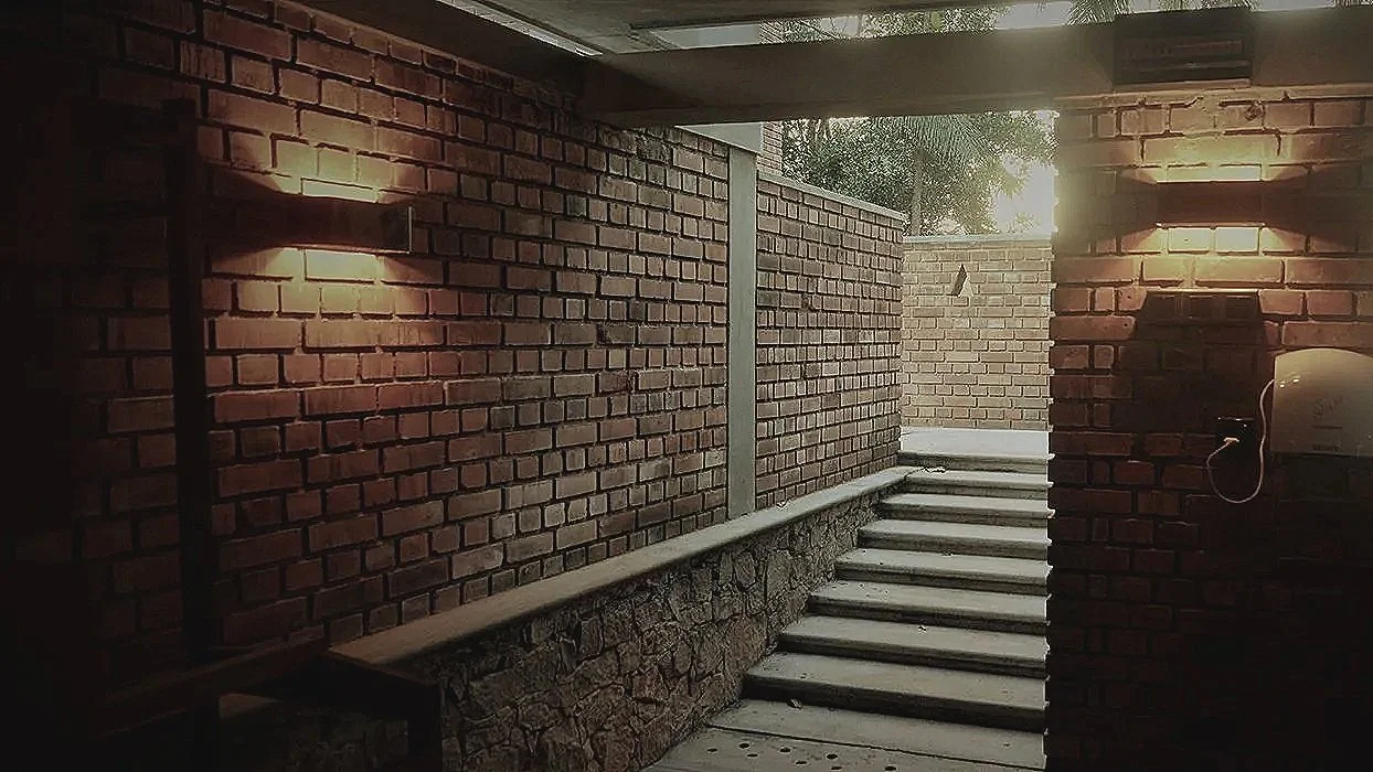 Outdoor brick staircase with brick walls on both sides, sunlight shining through an opening at the top, and a mailbox attached to the right wall.