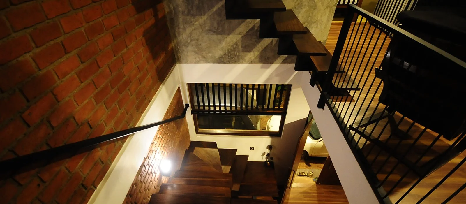 Interior view of a multi-story home with stairs, brick wall, and black metal railings, taken from the upper level looking down.