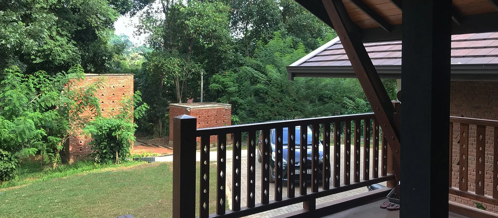 View from a porch showing greenery, brick walls, parked black car, and a small pathway.
