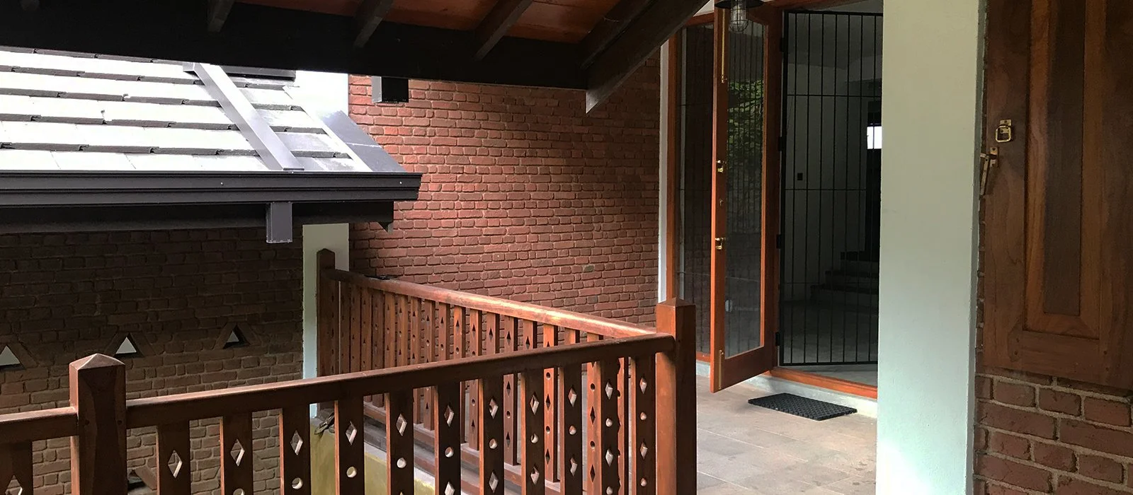 View of a brick and wood balcony with a door and security gate, part of a residential building exterior.