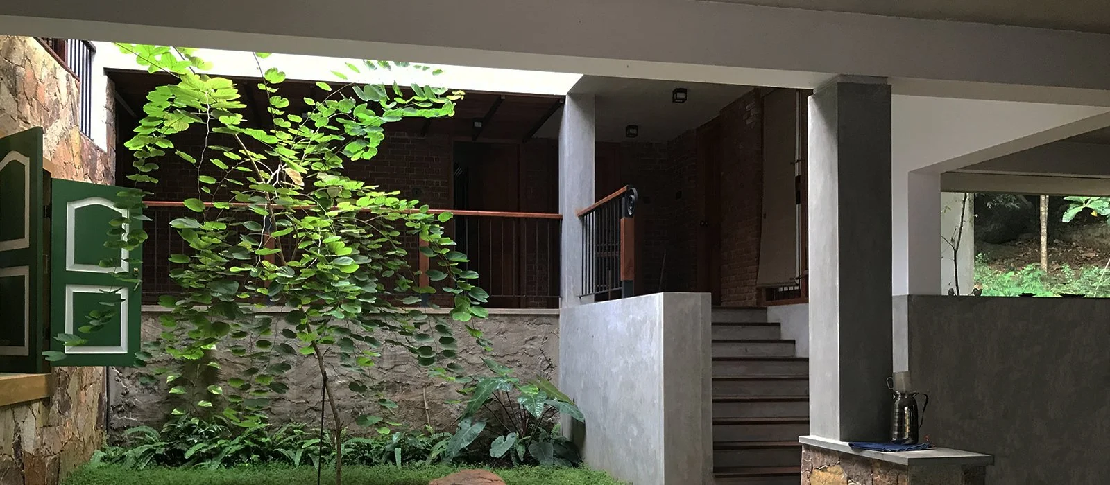 Interior view of a modern house with a small indoor garden, stairs, and a dark brick wall, seen from a covered patio area.