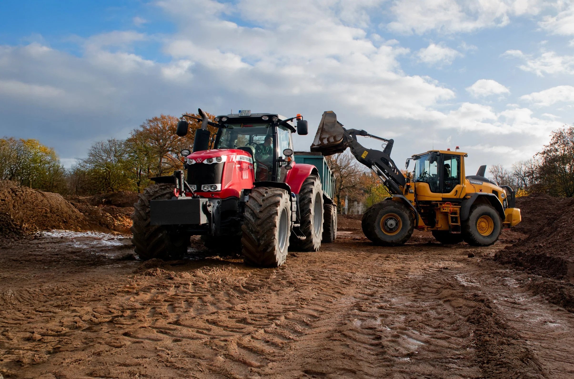Baufahrzeuge bei Bauarbeiten, ein roter Traktor und ein gelber Radlader auf einer Baustelle im Freien unter bewölktem Himmel.