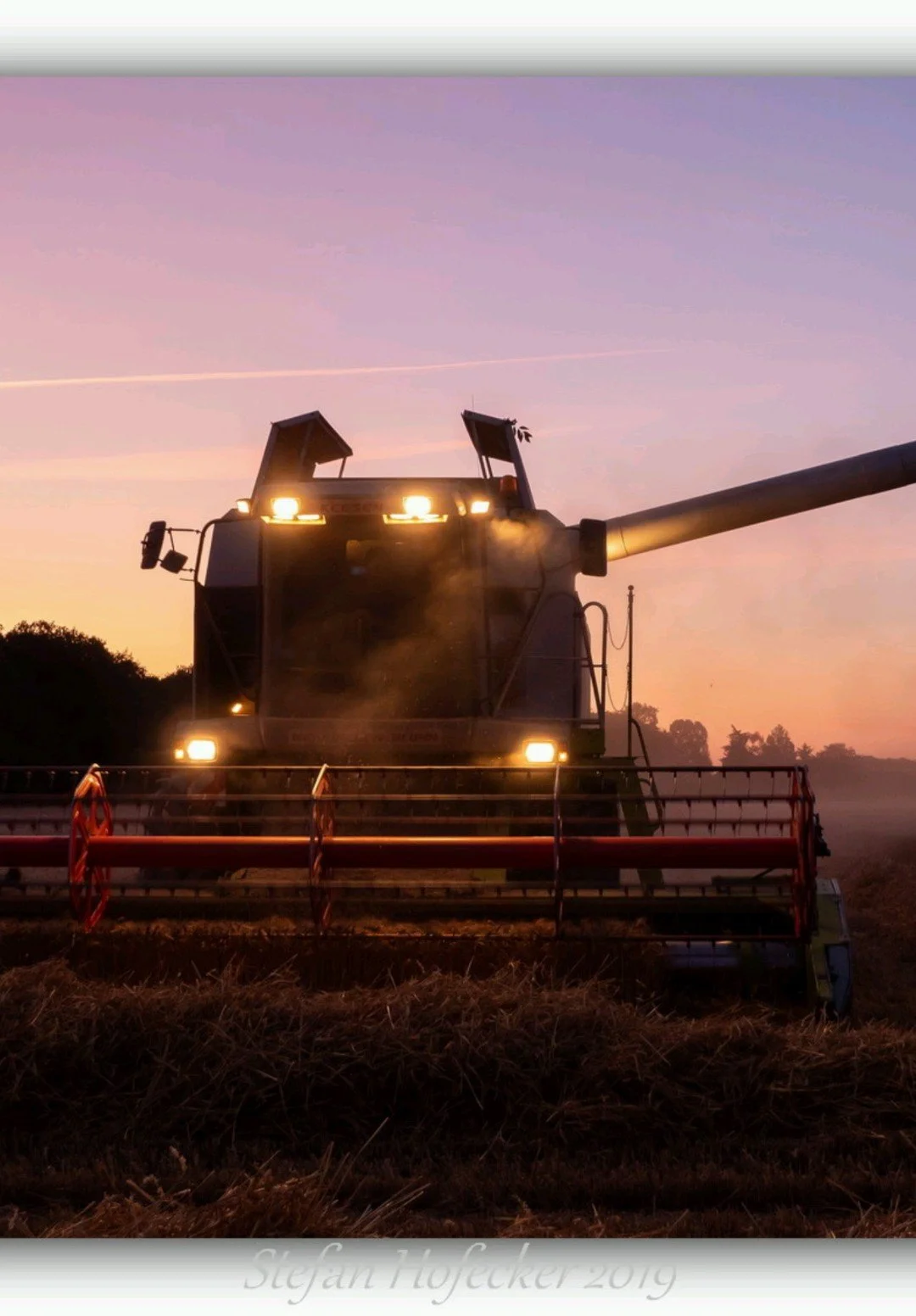 Ein landwirtschaftlicher Mähdrescher bei Sonnenaufgang oder Sonnenuntergang in einem Feld, Staub wirbelt auf.