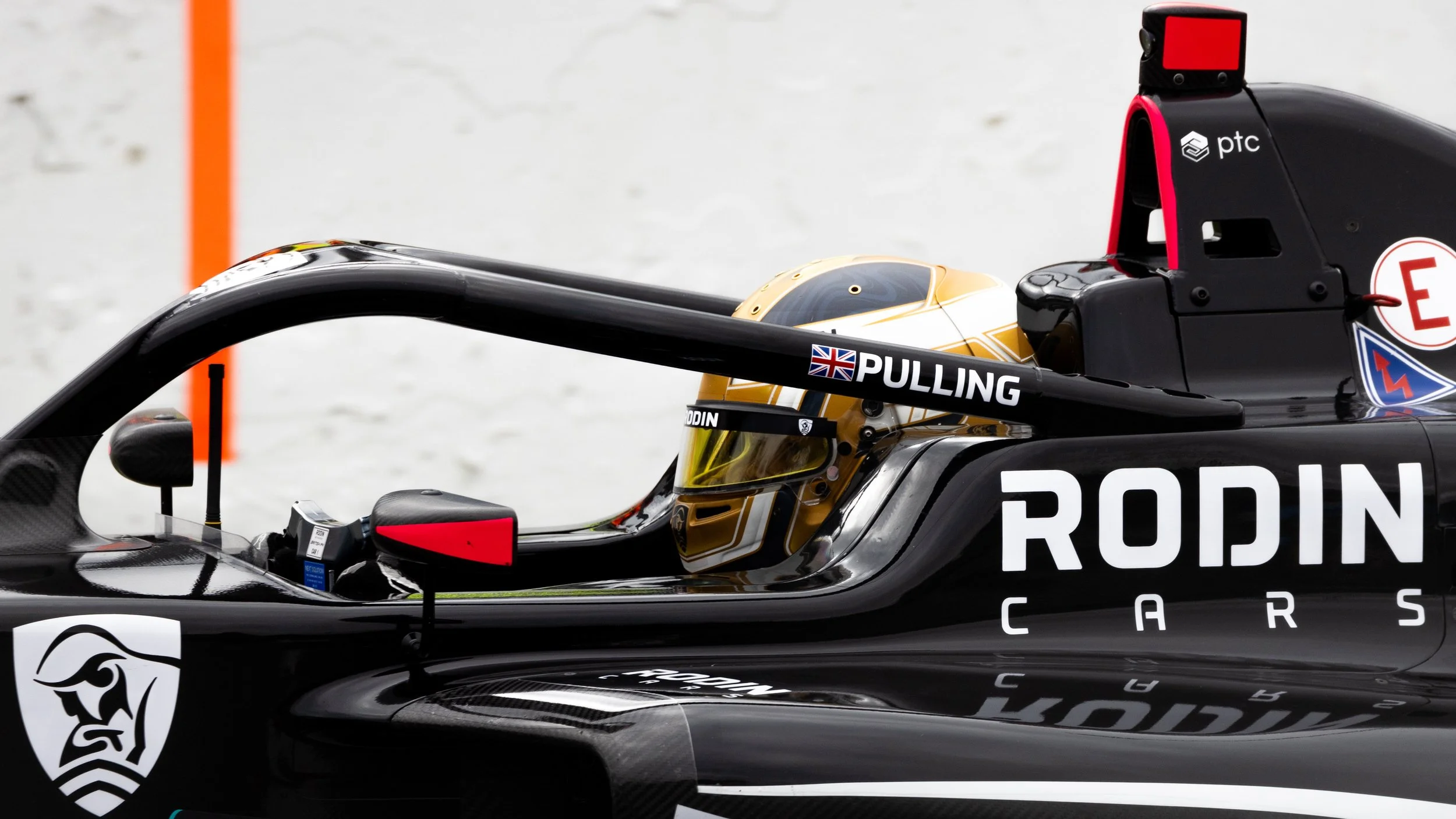Close-up of a black Formula E race car with a gold driver's helmet inside the cockpit, featuring various sponsor logos and the name 'RODIN CARS' on the side, on a race track.